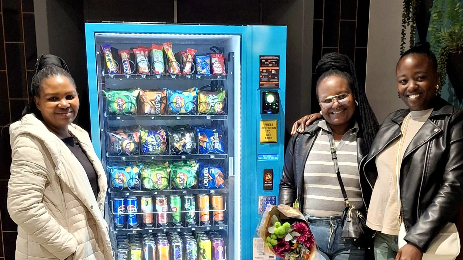 Three new vending machine owners standing beside their newly installed blue branded snack and drinks machine
