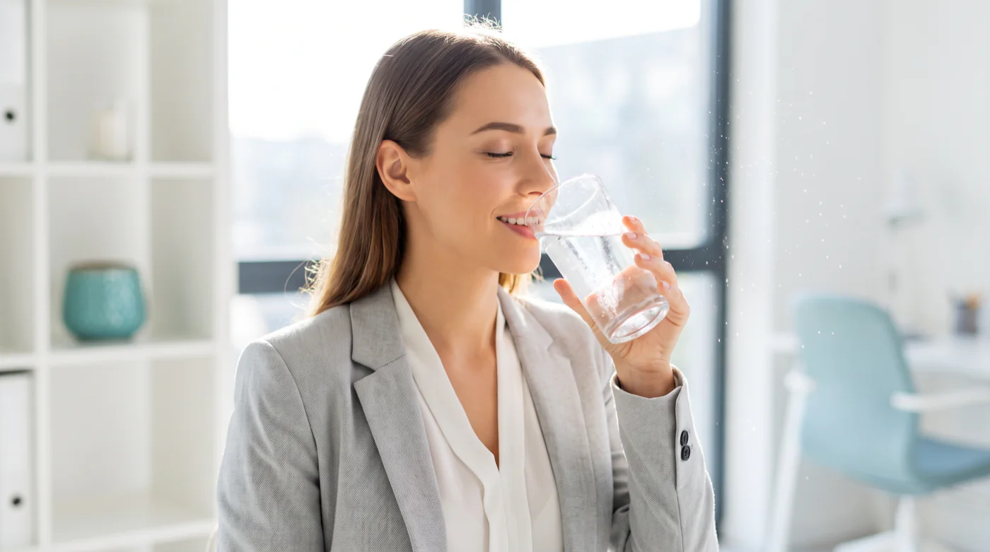 Woman drinking a glass of purified water in a bright office